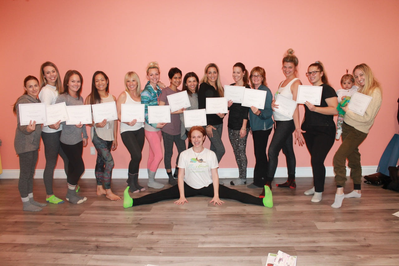 Kids Yoga Certification - Flow and Grow KIds Yoga Teacher Training with Instructor Lara Hocheiser. 15 women pose with their kids yoga certificates with instructor sitting on the floor in front of them