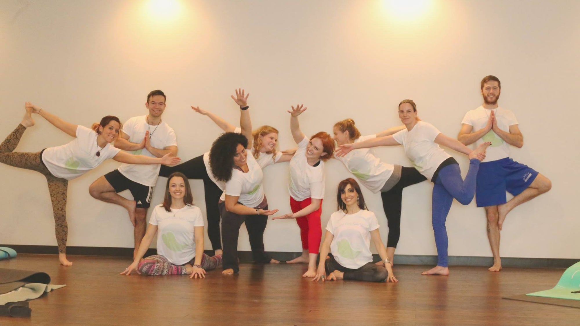A group of 10 adult learners at a yoga teacher training doing poses and smiling